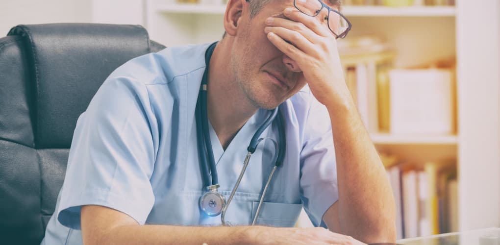 stressed physician sitting with head in hands while seated at desk