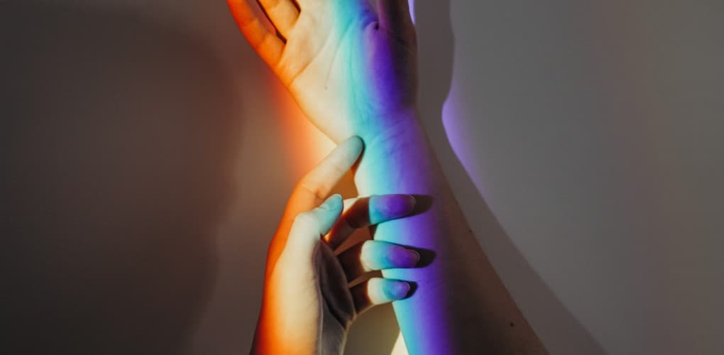 photo of human hands in rainbow light depicting caring for lgbtq patients